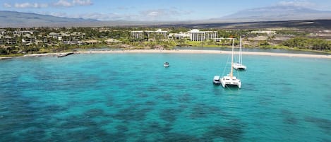 A coastal resort with clear turquoise waters, a sandy beach, and a backdrop of mountains.