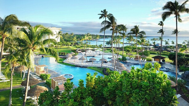 Een resort met een groot zwembad, palmbomen en uitzicht op de oceaan.