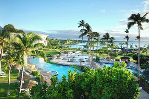 Un resort con una gran piscina, palmeras y vista al océano.