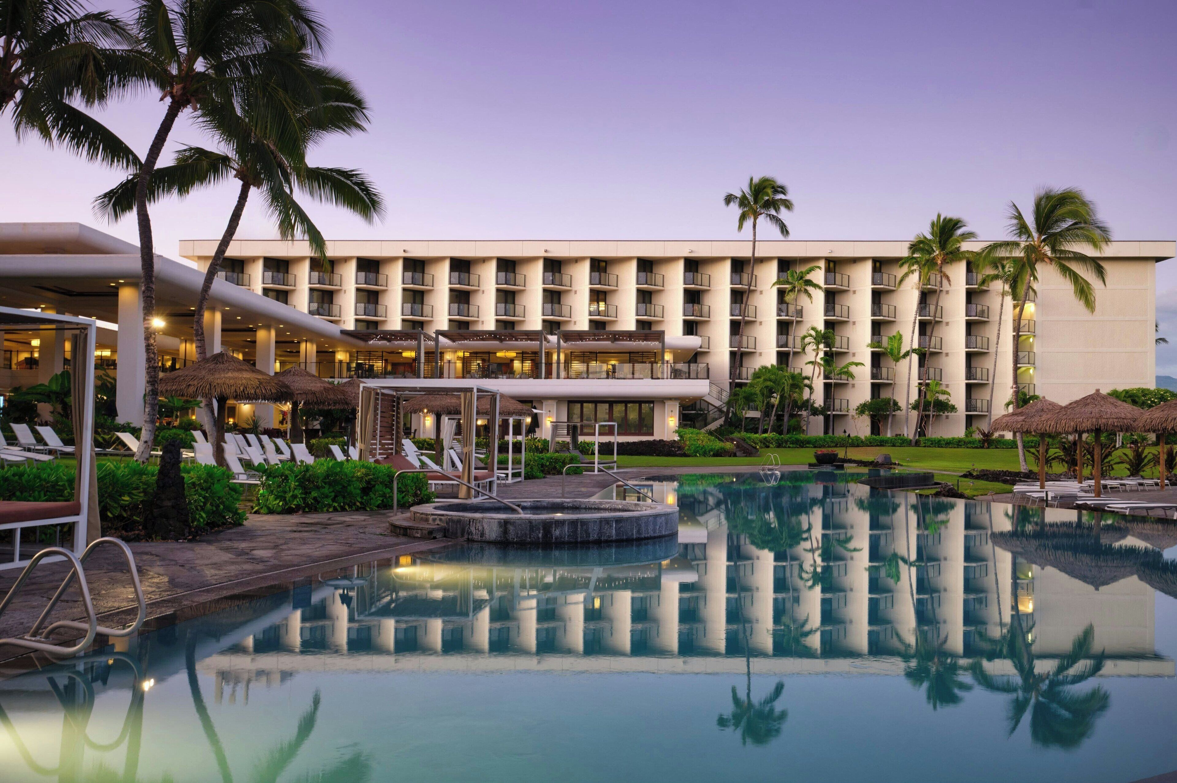 Un hotel con piscina, palmeras y una luminosa zona de recepción.