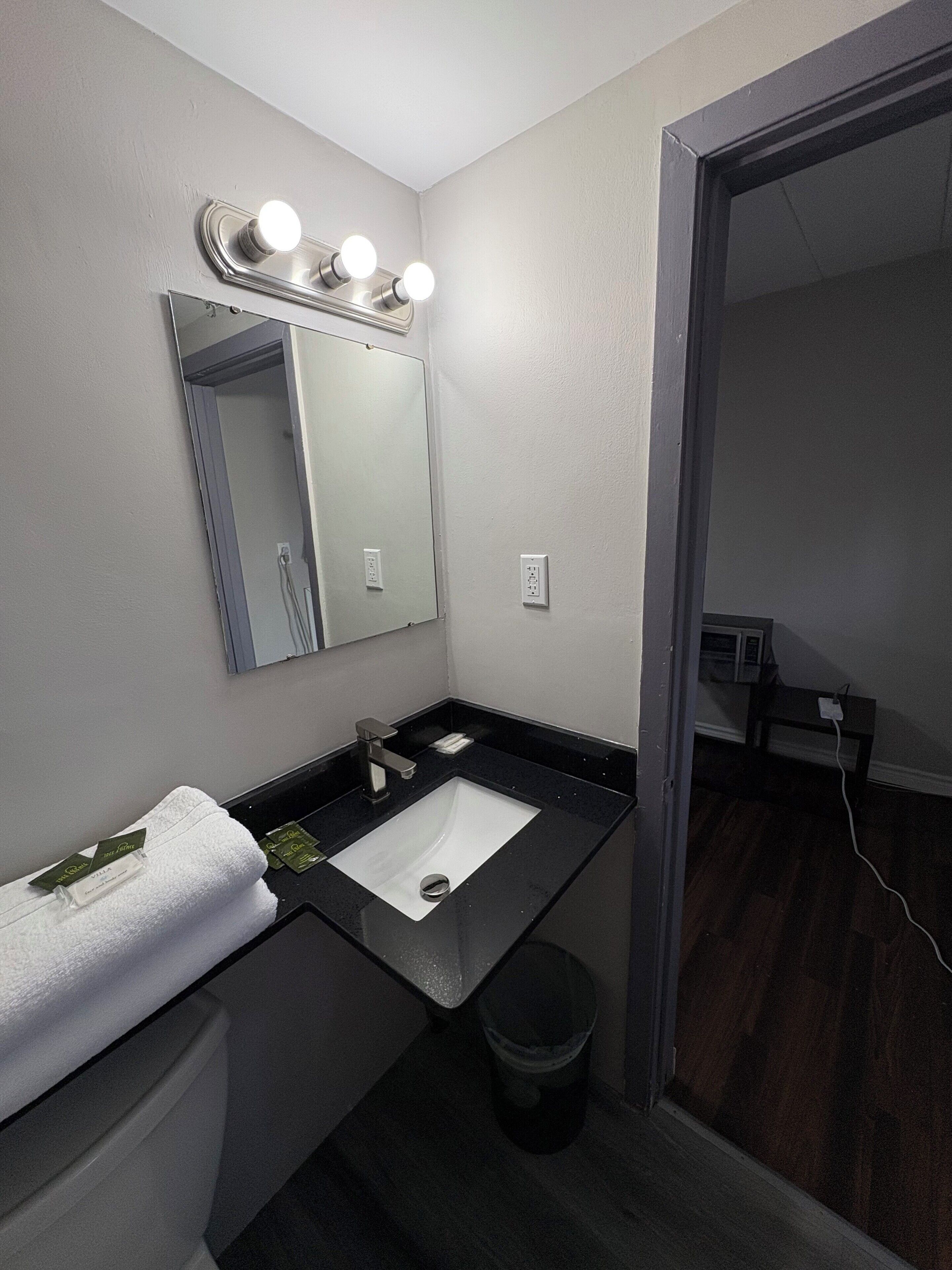 A modern bathroom with a black sink, a mirror with lights, a towel, and a trash can.