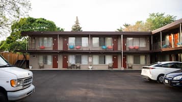 Un motel à deux étages, avec un parking et une voiture blanche garée devant.