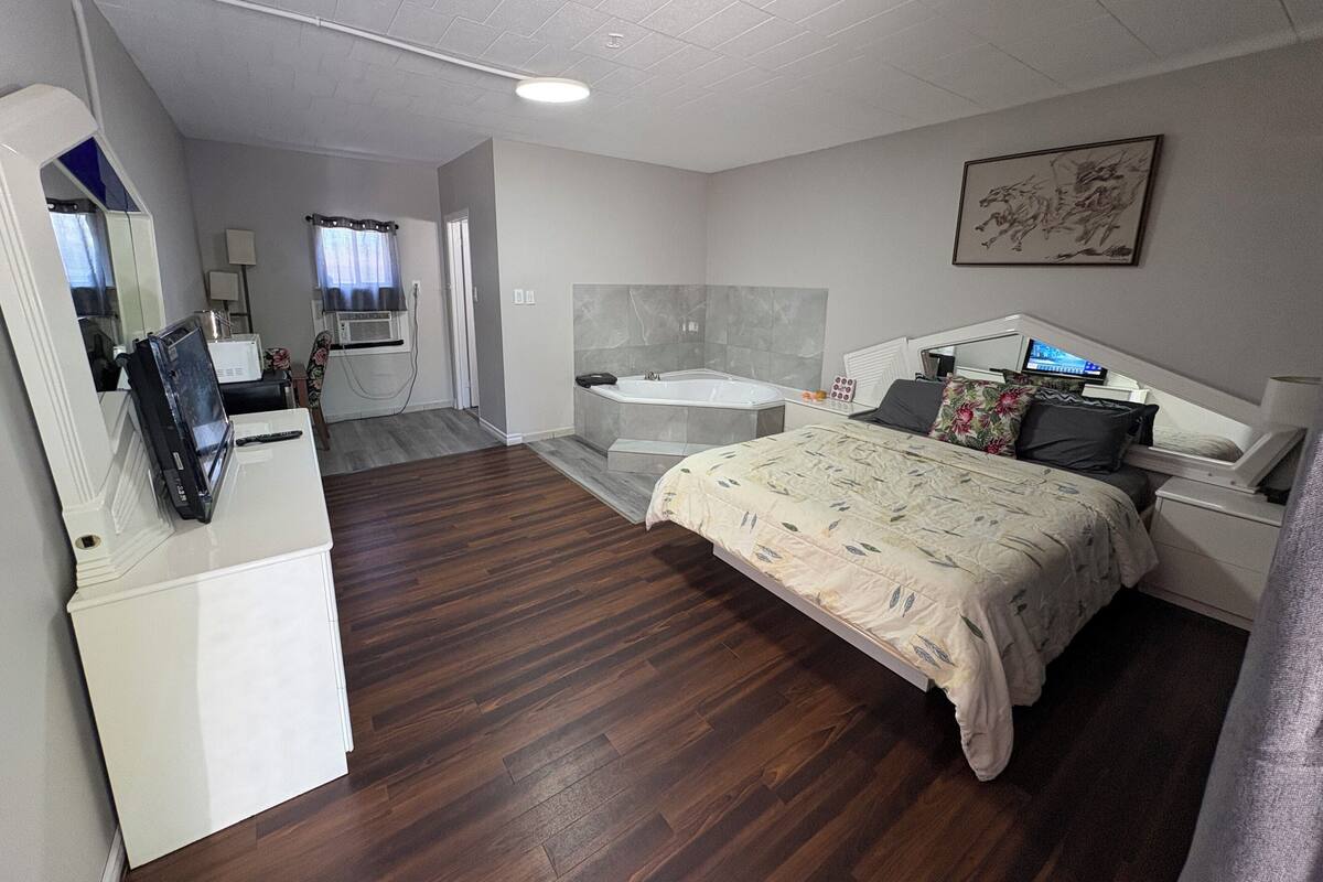 A bedroom with a bed, a desk, a chair, a TV, a bathroom with a bathtub, and a shower.