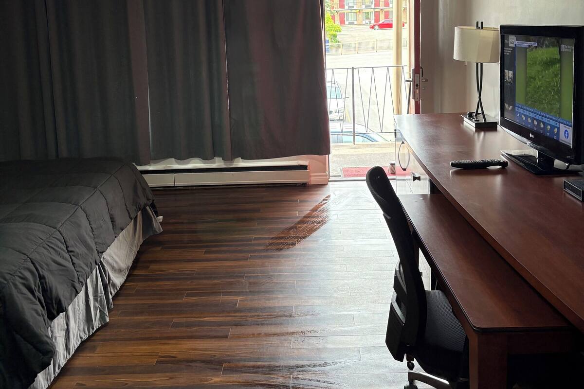 A hotel room with a bed, a desk with a computer, a chair, and a window with curtains.