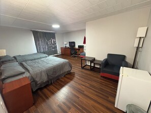 A hotel room with a bed, a desk, a chair, a television, and a lamp.