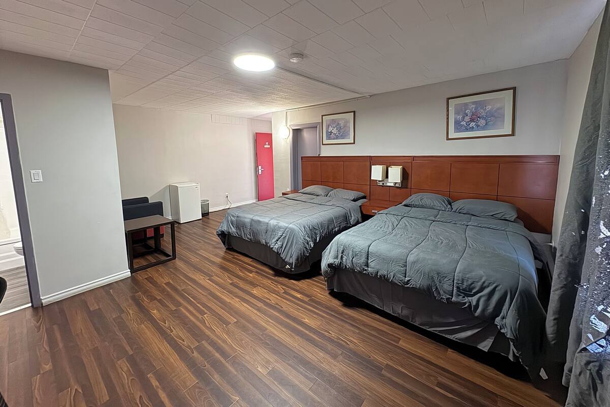 A hotel room with two beds, a desk, a refrigerator, and a red door.
