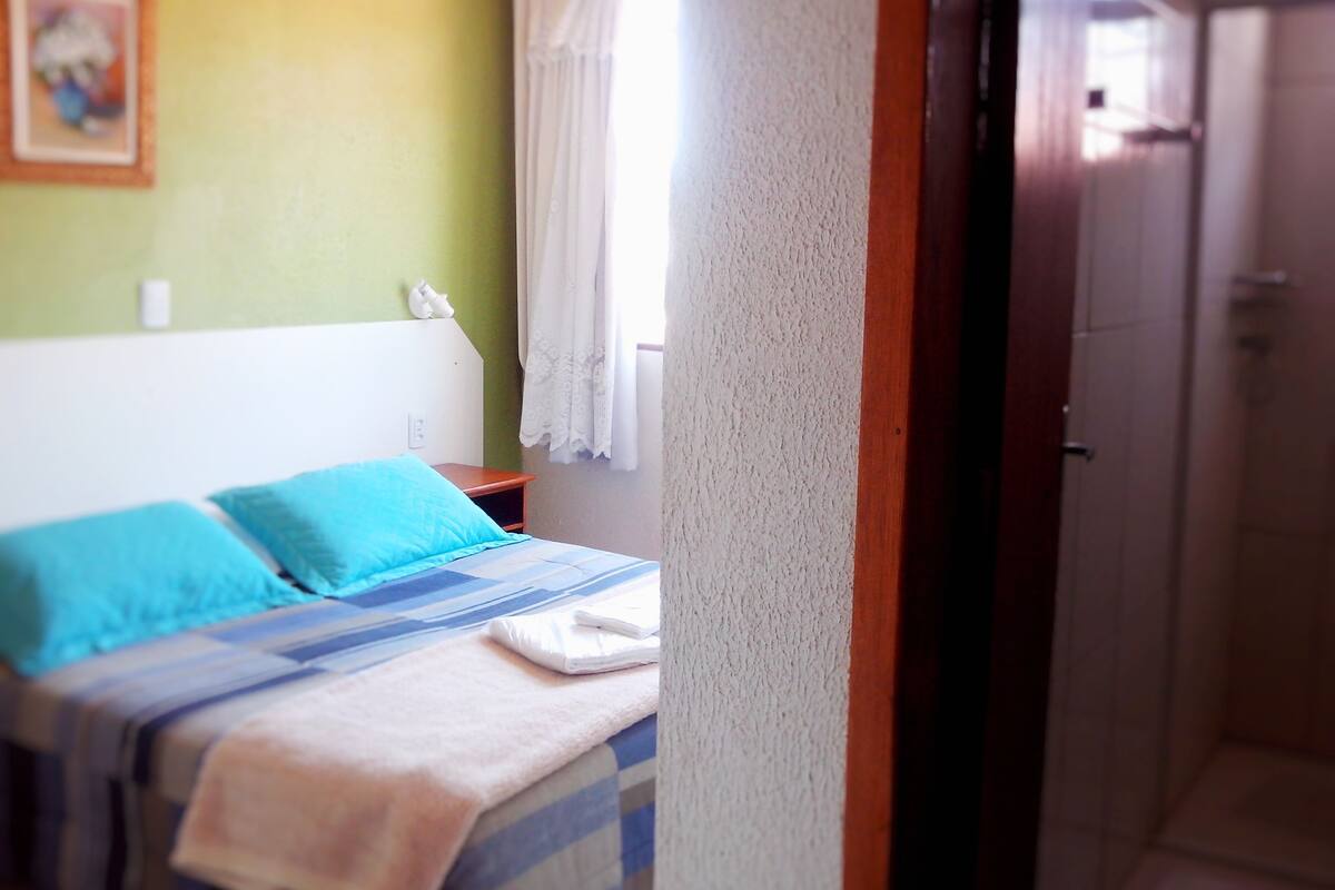 A bedroom with a bed, pillows, a nightstand, and a window with curtains.