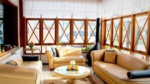 A sunlit living room with beige sofas, a round coffee table, and large windows with wooden frames.