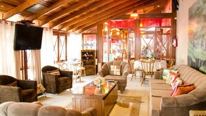 A spacious living area with wooden beams, comfortable seating, a television, and a wine rack.