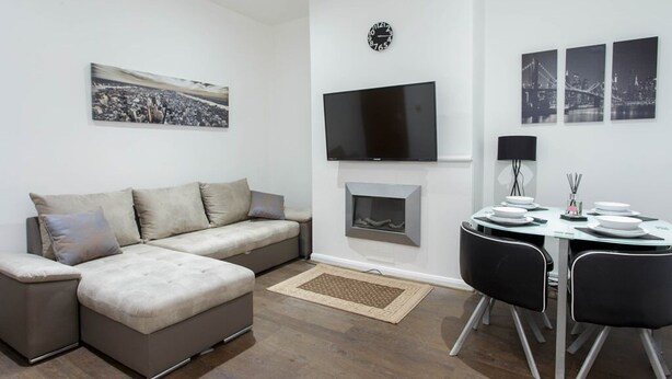 Uma sala de estar moderna com sofá, lareira, televisão de tela plana e um espaço de jantar com cadeiras e mesa.