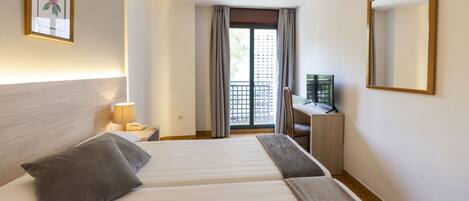 A hotel room with two beds, a desk, a chair, a TV, and a balcony with a view.
