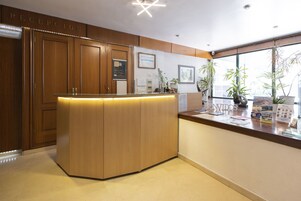Un área de recepción con armarios de madera, mostrador de recepción y ventana con plantas.