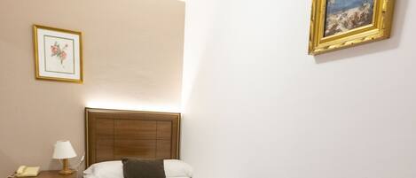 Habitación de hotel con una cama, una mesita de noche, una lámpara, un cuadro en la pared y suelo de baldosas.