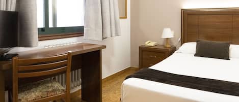 Una habitación de hotel con cama, escritorio, silla, mesita de noche y ventana con cortinas.