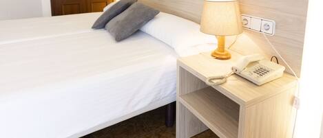 A hotel room with a bed, bedside table, lamp, phone, and a door.