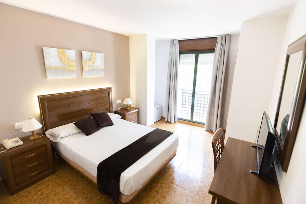 A hotel room with a large bed, a desk, a chair, a TV, a phone, and artwork on the wall.
