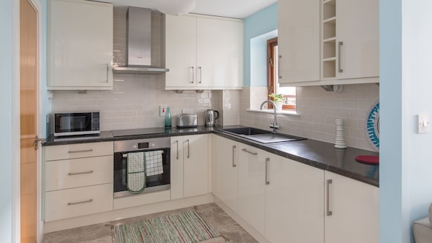 A modern kitchen with white cabinets, a stainless steel range hood, a microwave, a toaster, and a sink.