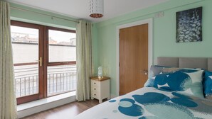 A bedroom with a bed, a nightstand, a wooden door, and a window with curtains.