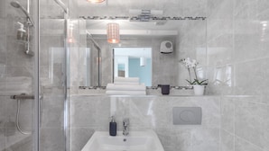 A modern bathroom with a glass shower enclosure, a white sink, and a towel rack.