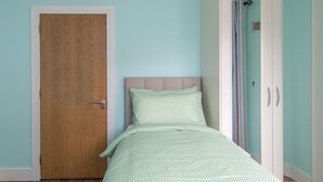 A bedroom with a wooden door, a bed with a patterned bedspread, and a wardrobe with a striped curtain.