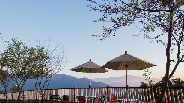 An outdoor seating area with tables and chairs, two umbrellas, and a view of mountains in the background. - Jia Maei B&B (Ren'ai)