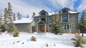 Un chalet à deux étages avec une façade en pierre, une porte d’entrée en bois et un toit recouvert de neige.
