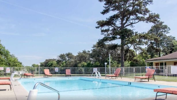 Una piscina rectangular con una escalera de metal, rodeada de sillas de descanso rojas y una cerca metálica.