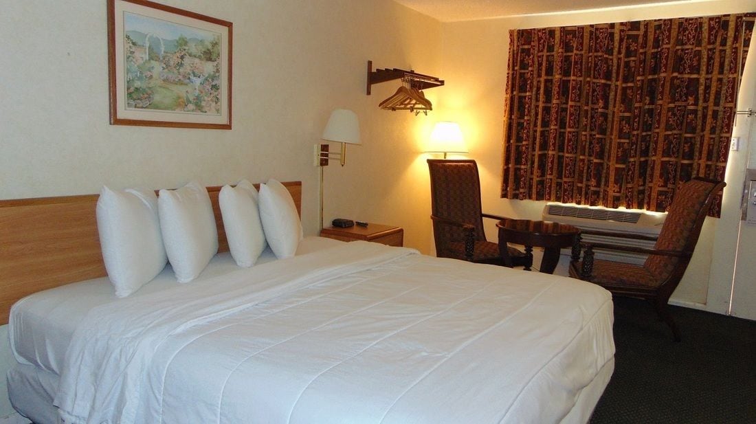A hotel room with a large bed, a desk, a chair, a lamp, and a painting on the wall.