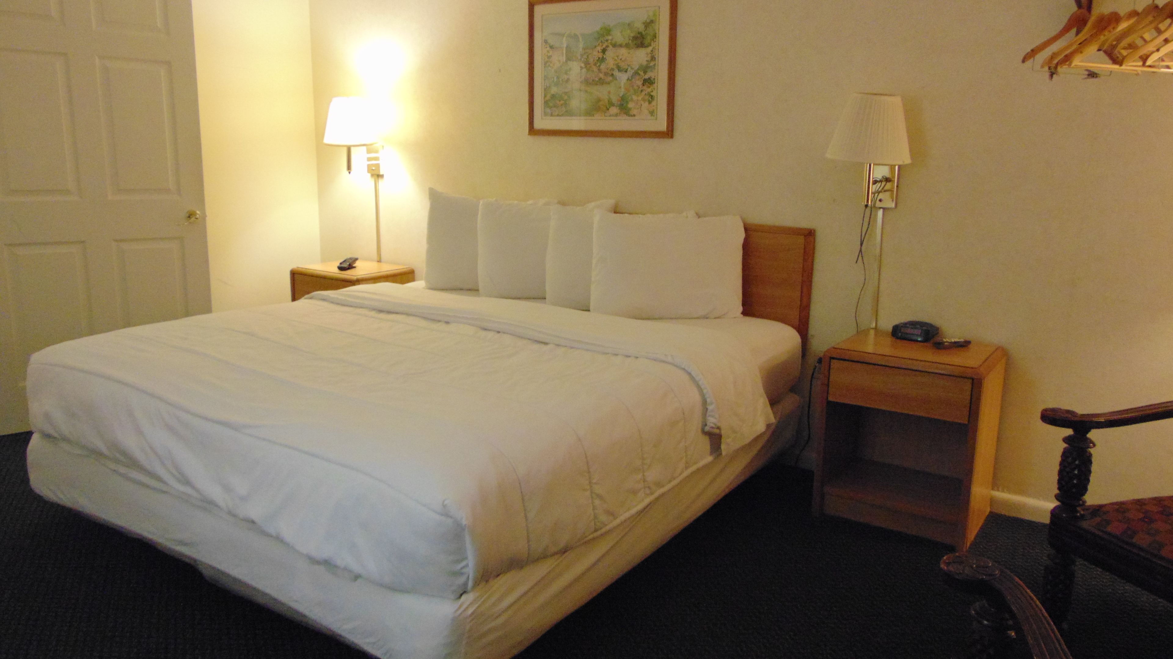 A neatly made bed with white linens, two bedside tables with lamps, a framed picture on the wall, and a chair in the corner.