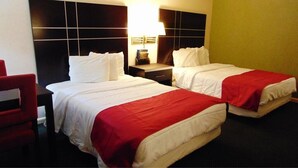 Habitación de hotel con dos camas, una silla roja, una mesita de noche con lámpara y un reloj en la pared.
