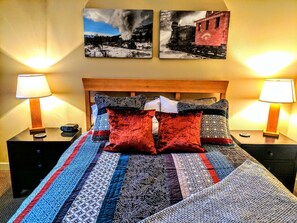 A neatly made bed with patterned bedding and two red pillows, flanked by two bedside tables with lamps and clocks, in a room with a wooden headboard and two framed pictures on the wall. - Founders Pointe 4457 2 Bedroom Holiday Home by Winter Park Lodging Company (Winter Park)