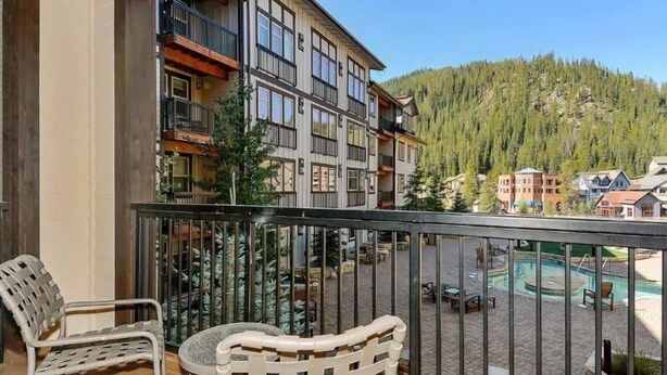 A balcony with two chairs and a table, overlooking a pool area and a forested hillside. - Founders Pointe 4457 2 Bedroom Holiday Home by Winter Park Lodging Company (Winter Park)