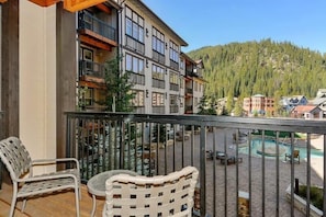 A balcony with two chairs and a table, overlooking a pool area and a forested hillside. - Founders Pointe 4457 2 Bedroom Holiday Home by Winter Park Lodging Company (Winter Park)