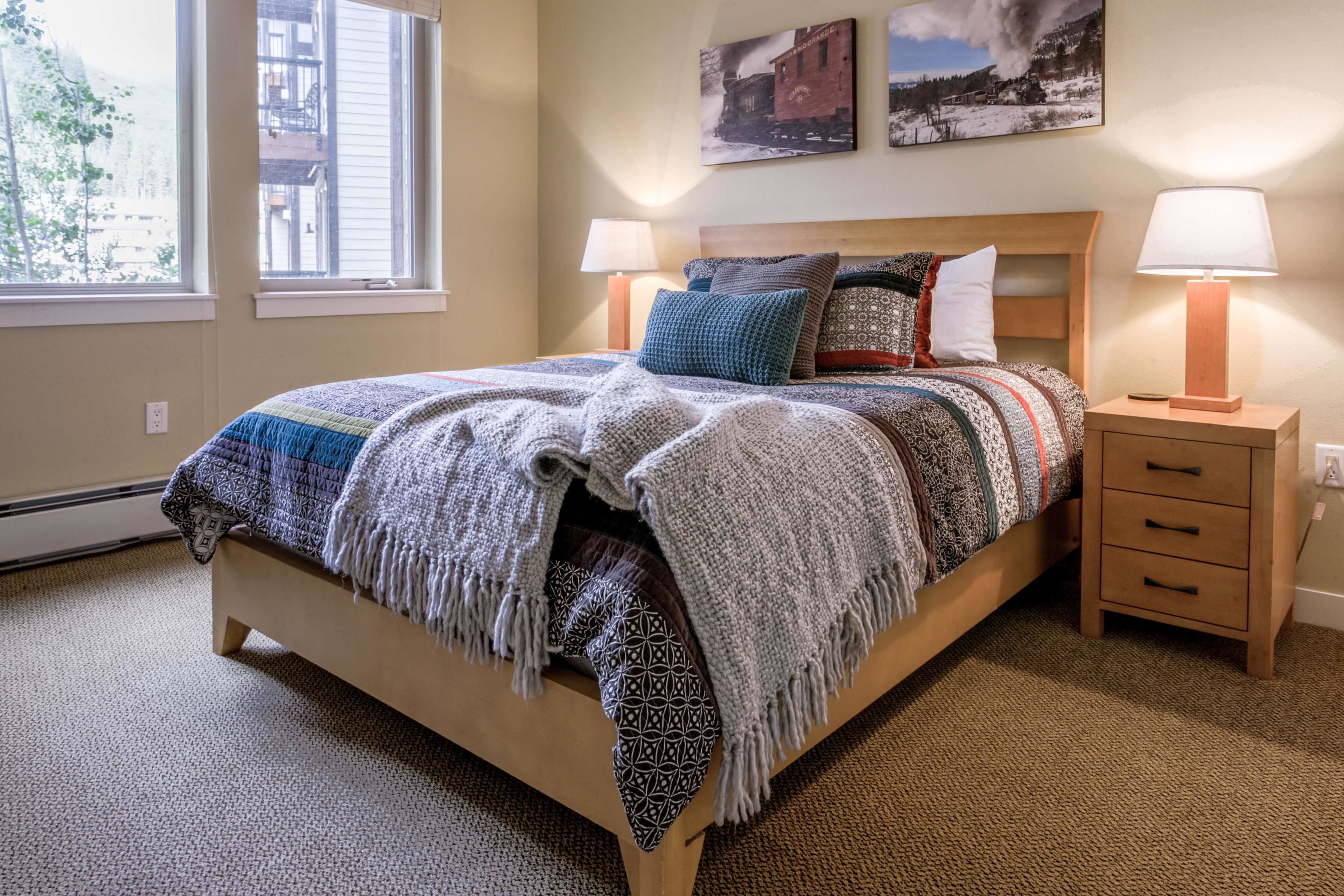 A neatly arranged bedroom with a large bed, two bedside tables with lamps, patterned bedding, and two wall-mounted pictures.