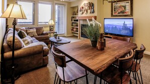 A living room with a sofa, a wooden dining table, chairs, a television, a fireplace, and a ceiling fan. - Founders Pointe 4457 2 Bedroom Holiday Home by Winter Park Lodging Company (Winter Park)
