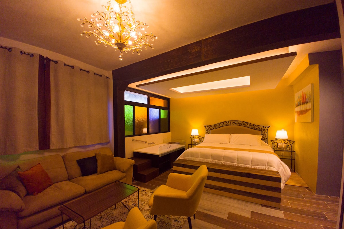 A hotel room with a bed, a sofa, a chair, a desk, and a chandelier.