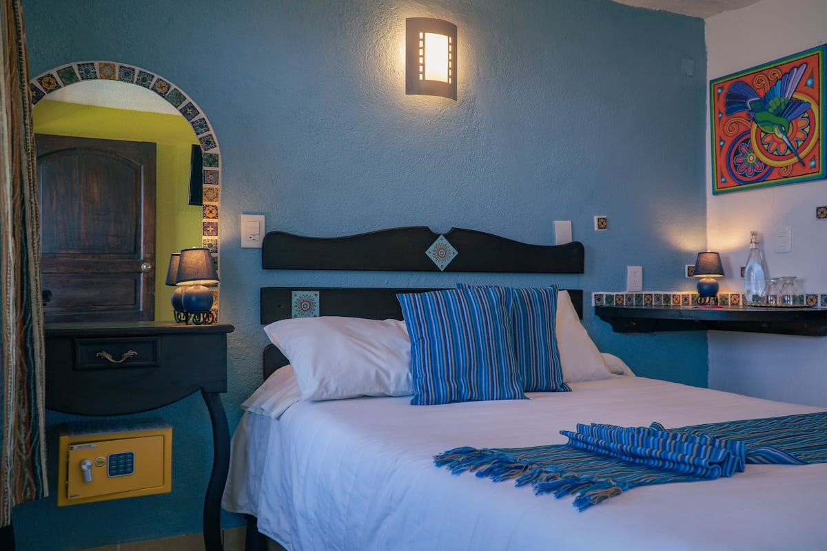 A bedroom with a bed, bedside lamps, a nightstand, a safe, and a decorative wall piece.