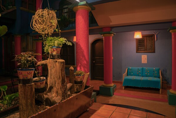 A lobby with a wooden planter, a blue sofa, and a hanging light fixture. - Hotel Tepeyac (San Cristóbal de las Casas)