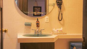 A bathroom with a sink, mirror, hairdryer, and toiletries.