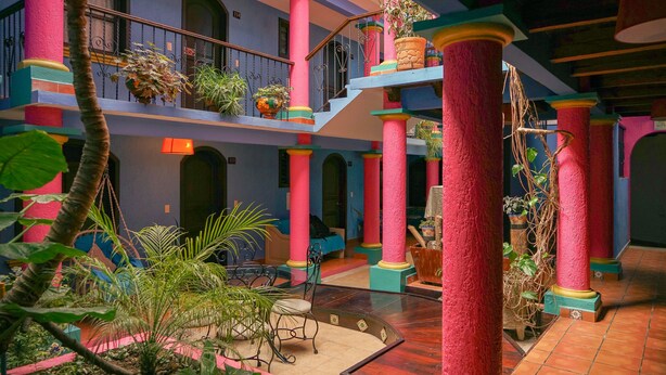 A multi-level atrium with vibrant pink and blue columns, a staircase, and indoor plants. - Hotel Tepeyac (San Cristóbal de las Casas)