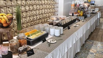 Ein reichhaltiges Buffet mit verschiedenen Speisen, darunter Obst, Joghurt und Nüsse, präsentiert auf einem langen Tisch mit einem gemusterten Boden.