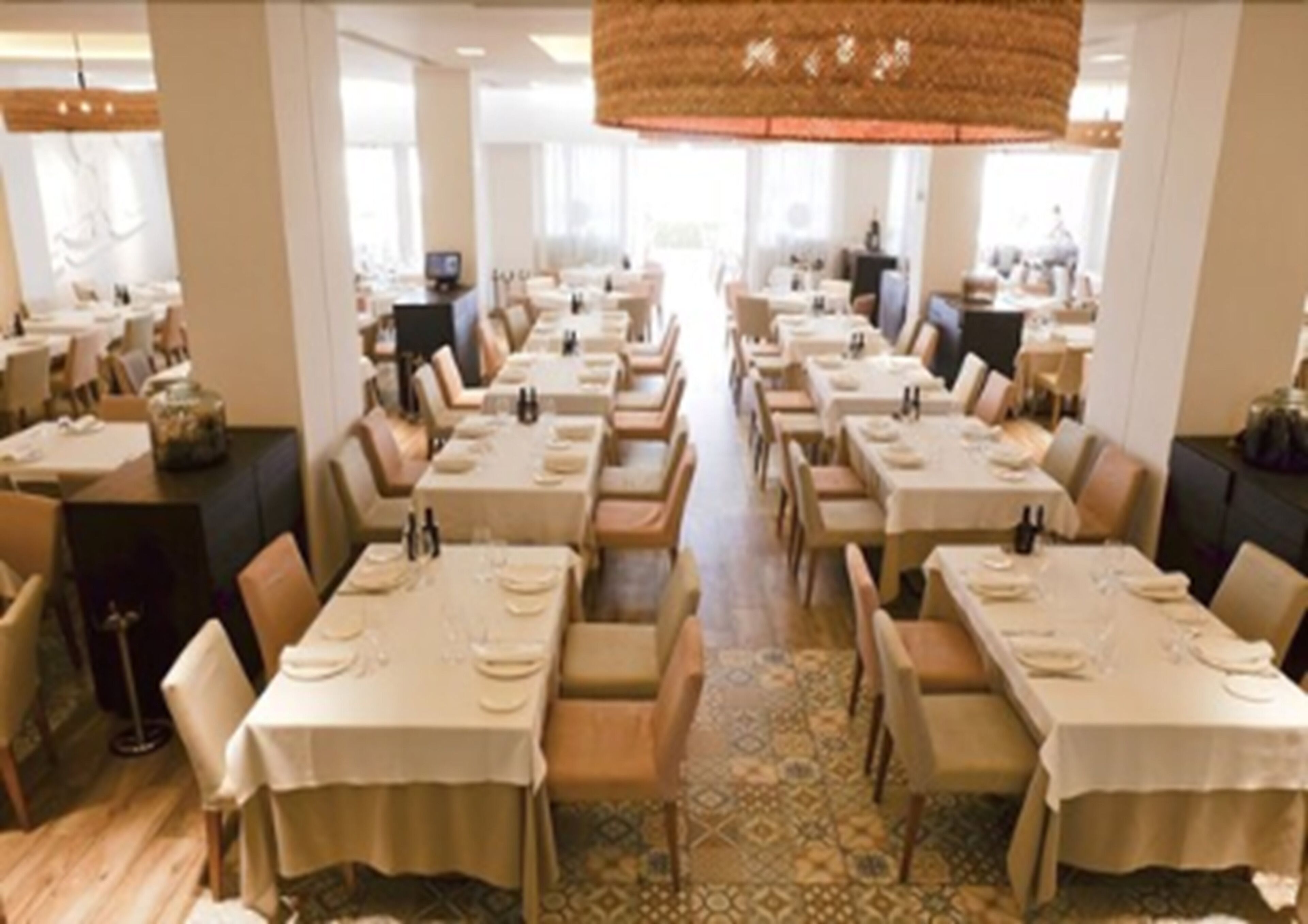 Un comedor amplio con varias mesas dispuestas para el servicio, un suelo con estampado y una lámpara colgante grande.