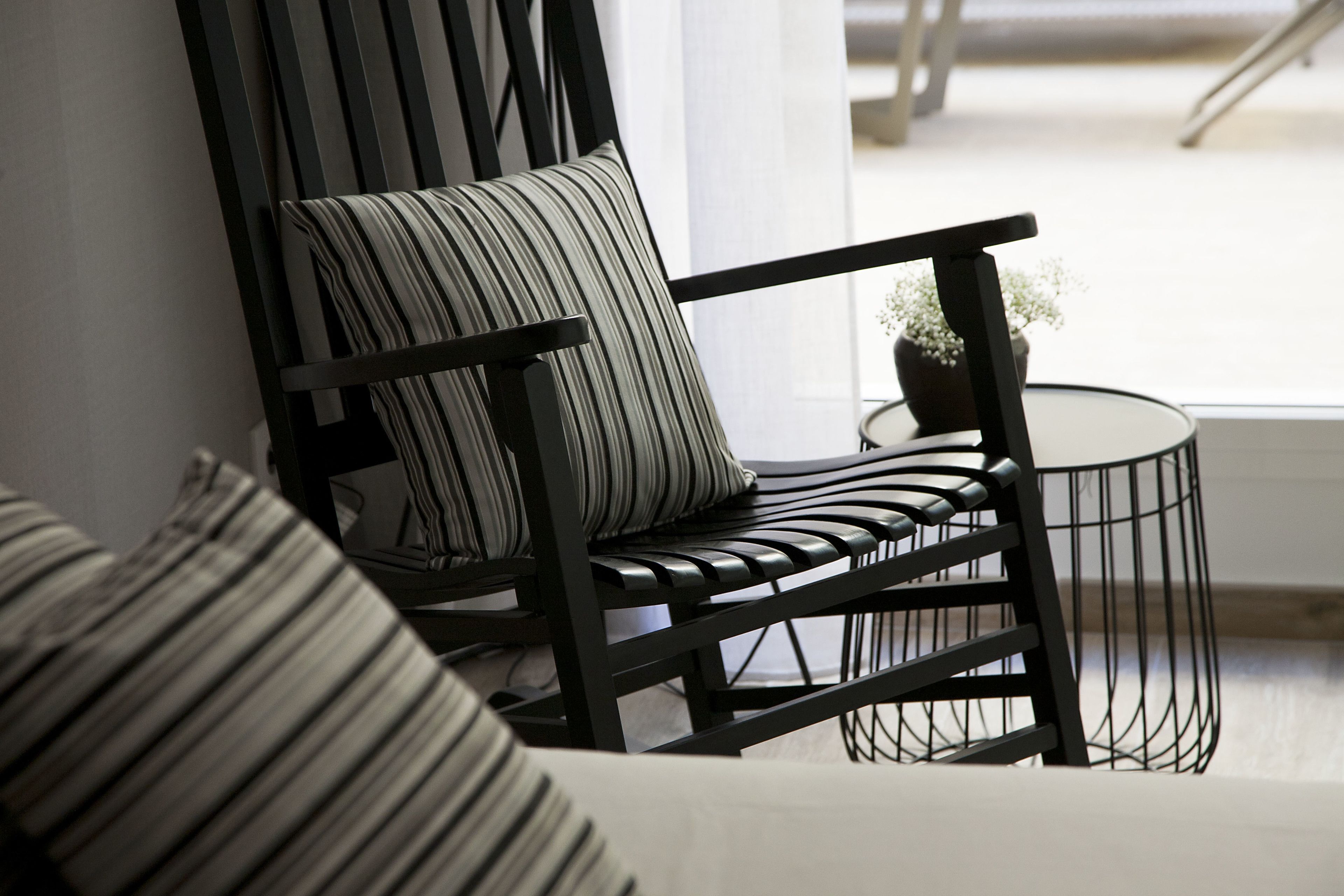 Una silla moderna con un cojín a rayas, una mesita redonda con una planta, y vista a una escalera.