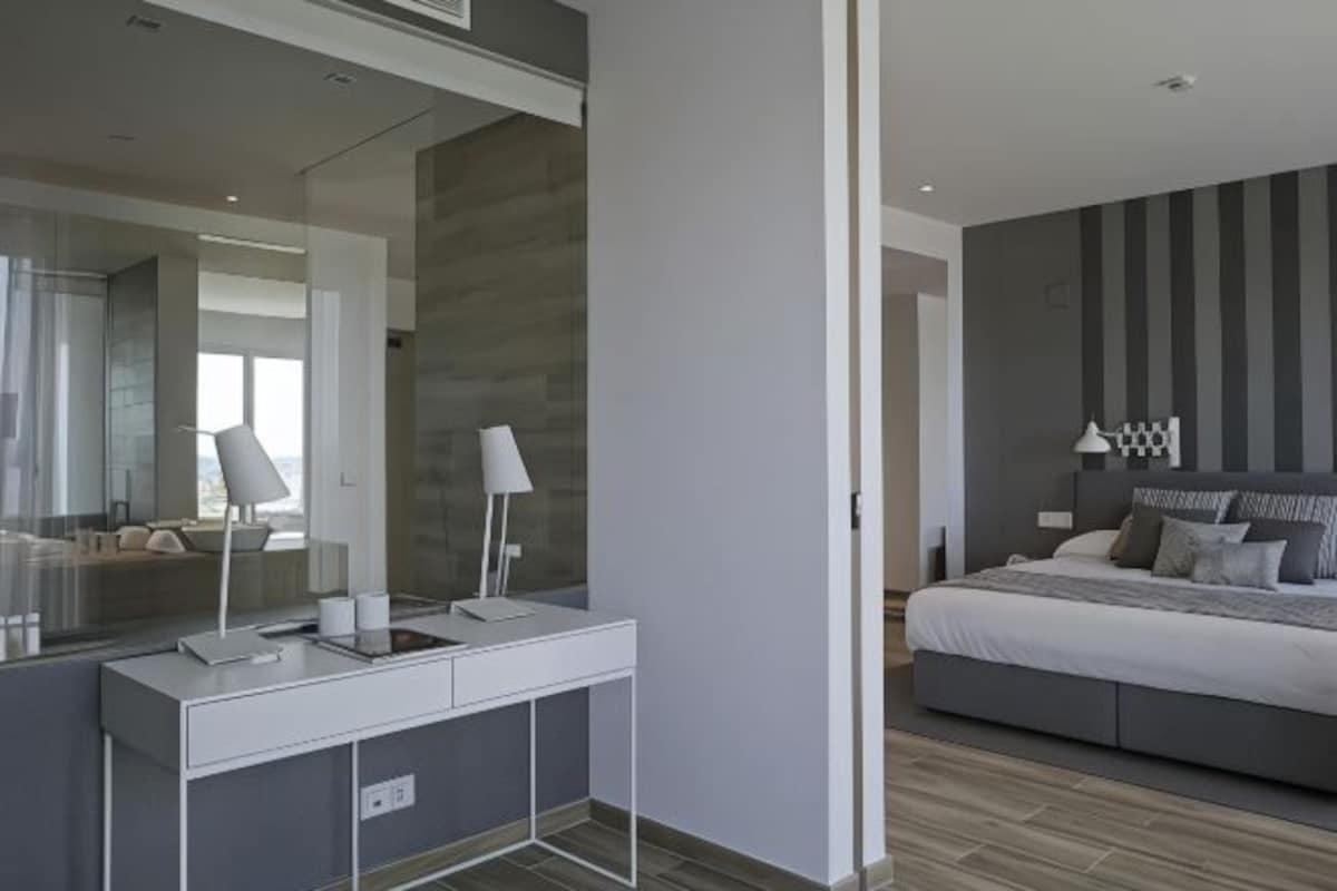 A modern bedroom with a large bed, a bedside table with lamps, and a large mirror.