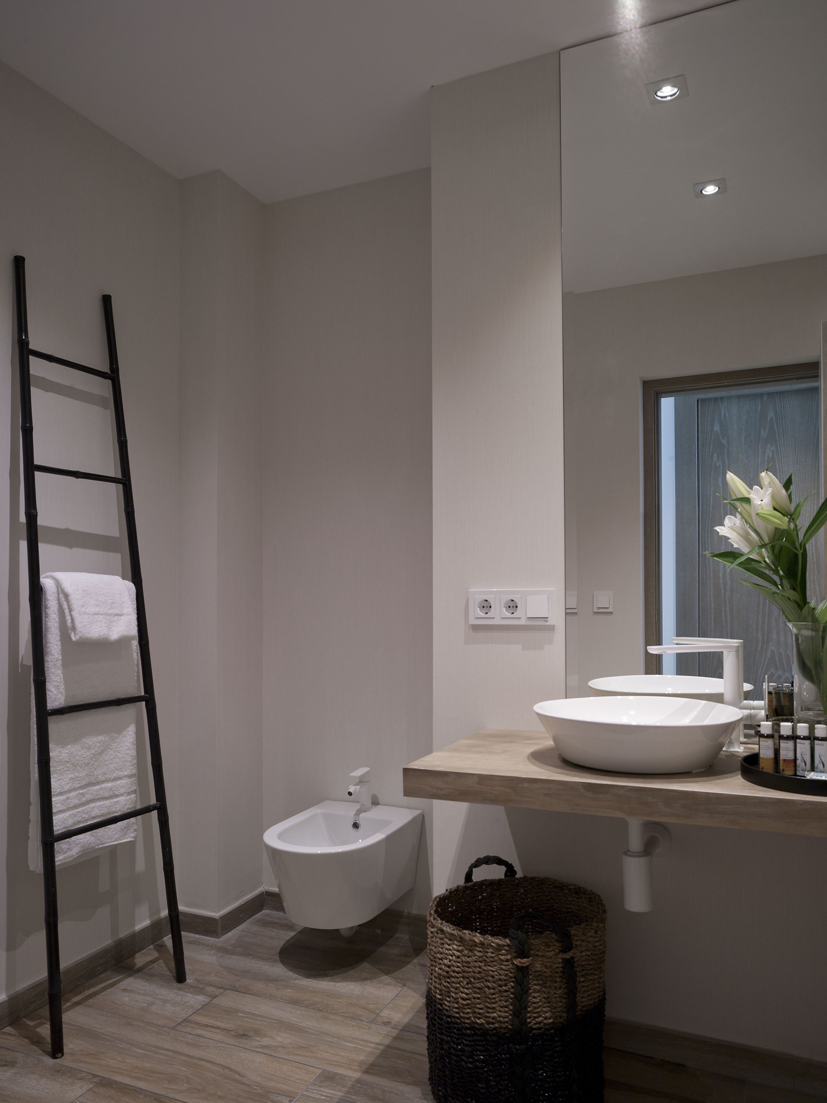 A modern bathroom with a white sink, a bidet, a mirror, and a black ladder.