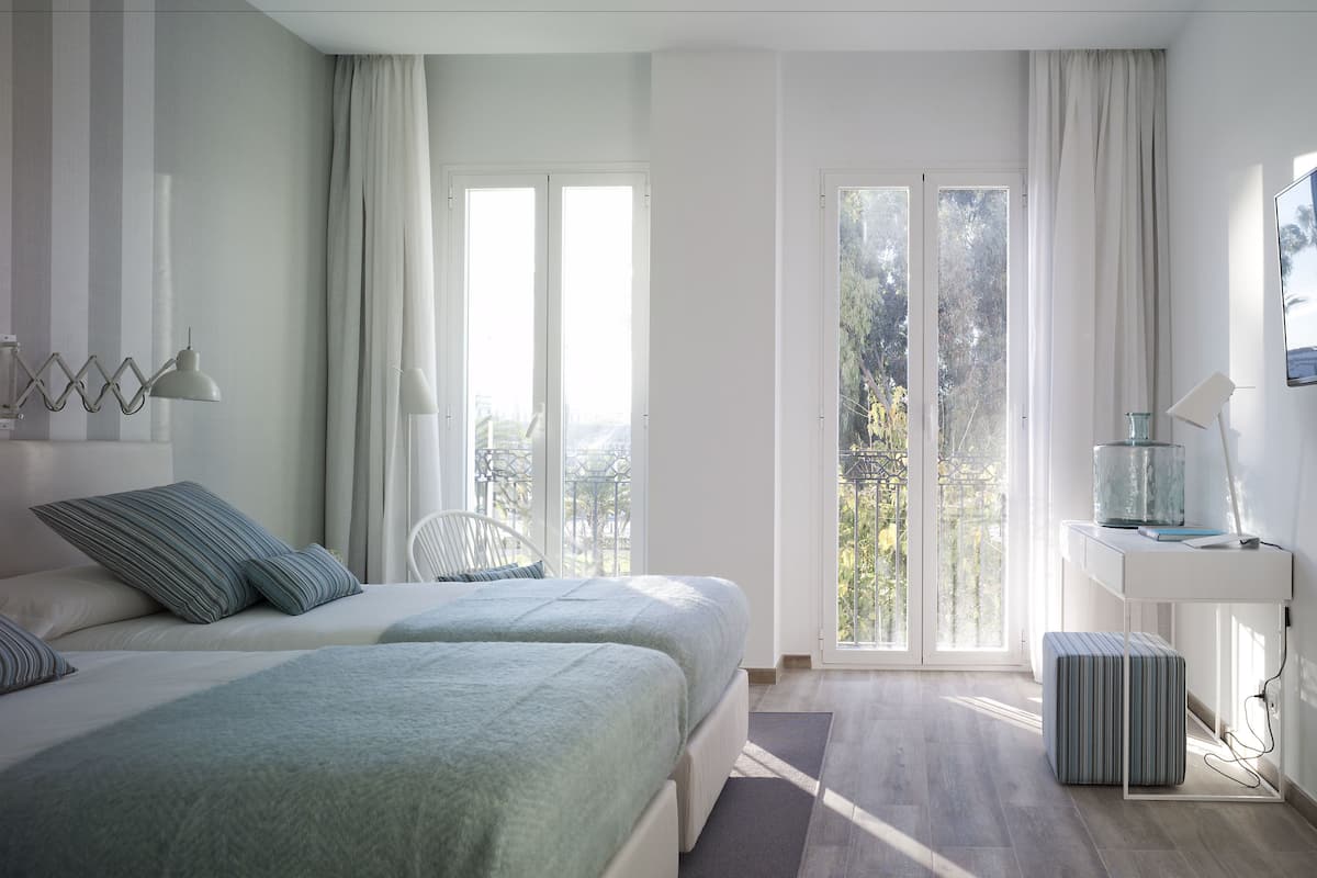 A modern bedroom with two beds, a large window, and a view of the outdoors.