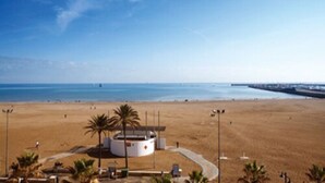 Vista de una playa con un edificio circular, palmeras y cielo despejado.