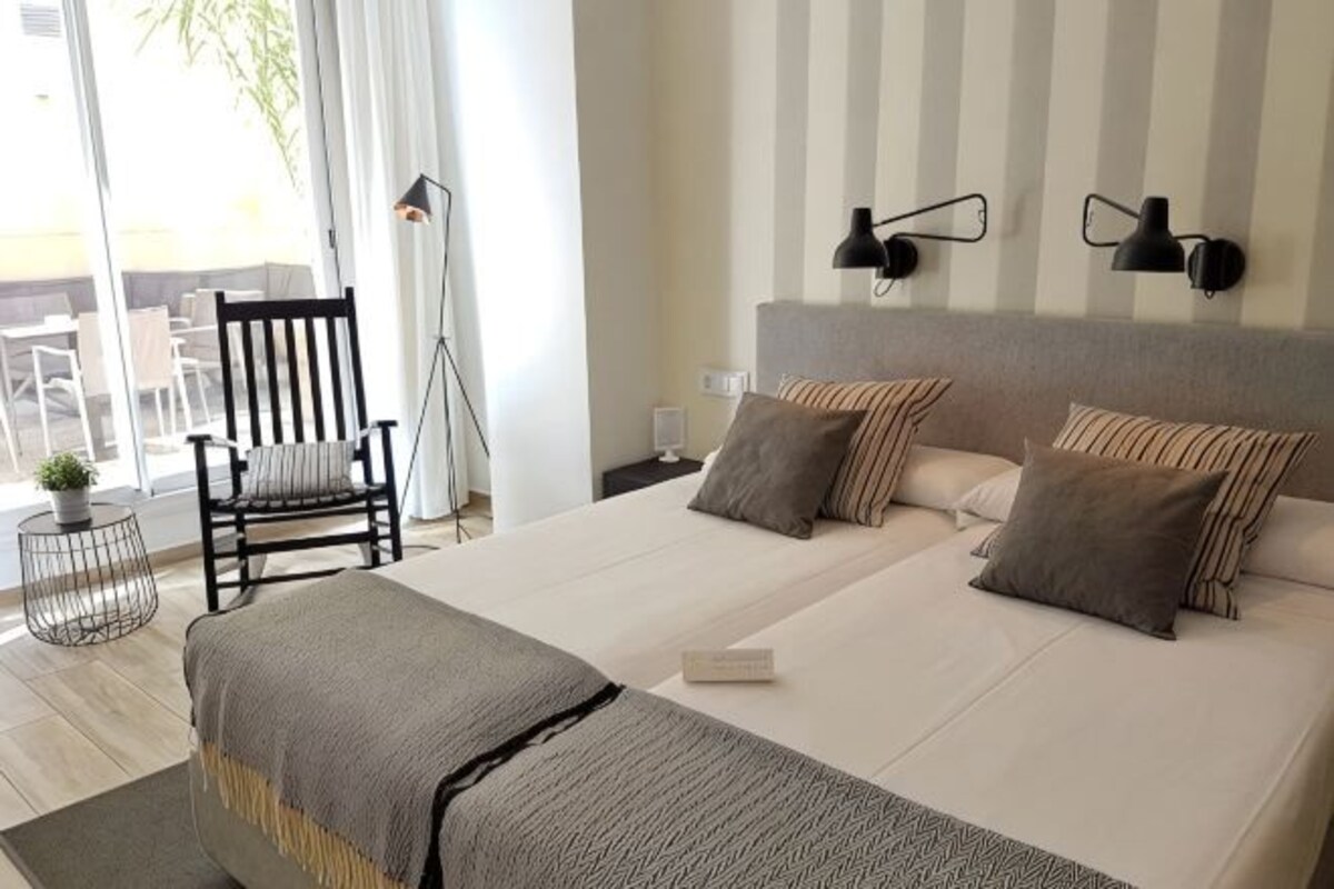 A hotel room with a large bed, two bedside tables, a chair, a floor lamp, and a view of the outdoors.