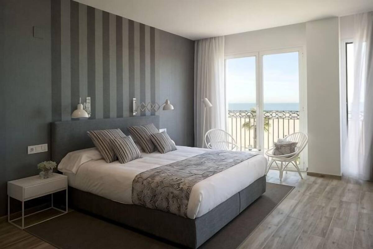 A modern bedroom with a large bed, bedside tables, a chair, and a balcony with a view.