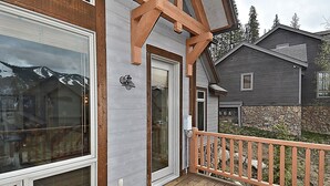 Une terrasse en bois avec une fondation en pierre, une porte dotée d’un panneau de verre et une vue sur une chaîne de montagnes.